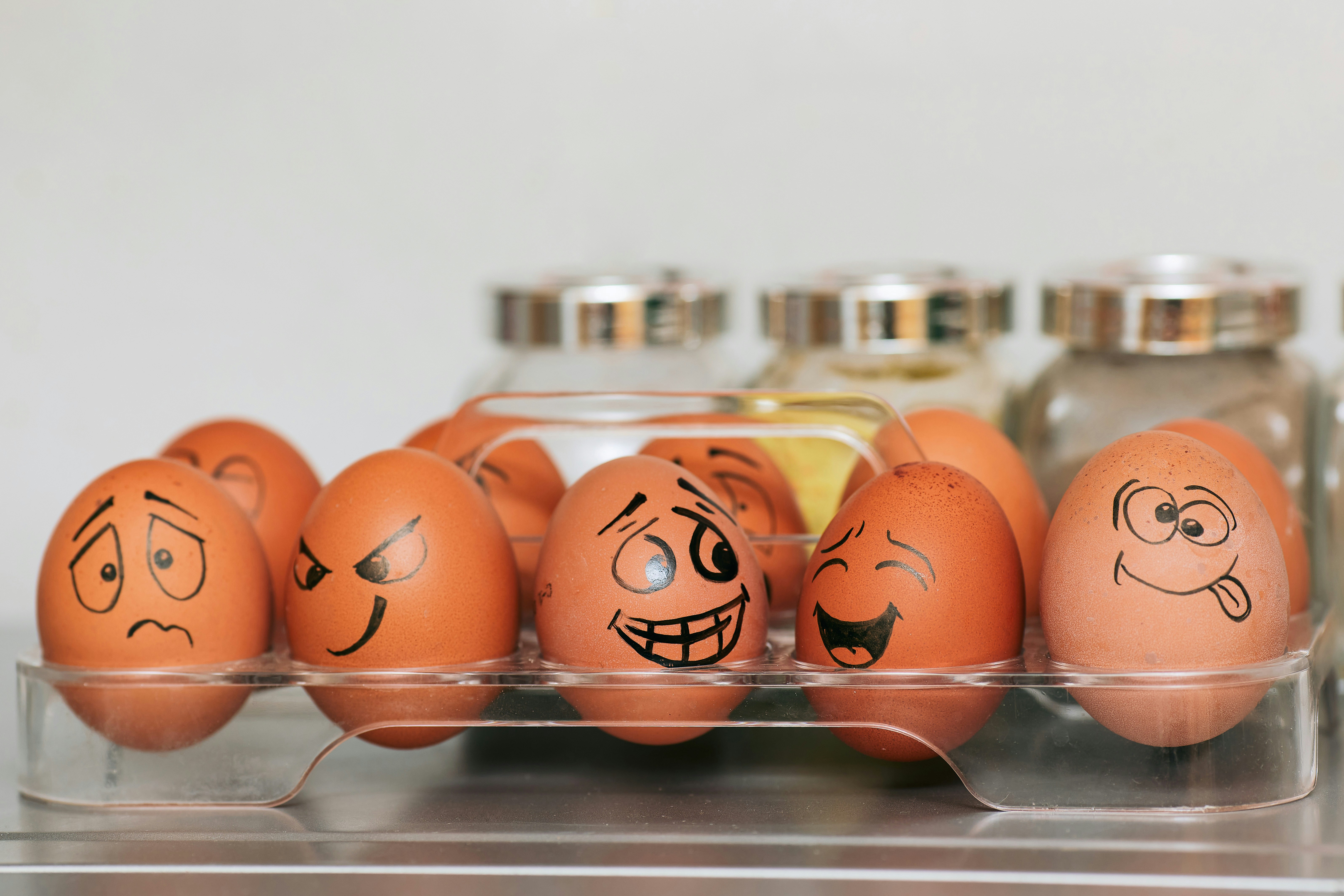 A photograph of whole painted eggs with different emotions against a background of blurred spices and a smooth gray wall.